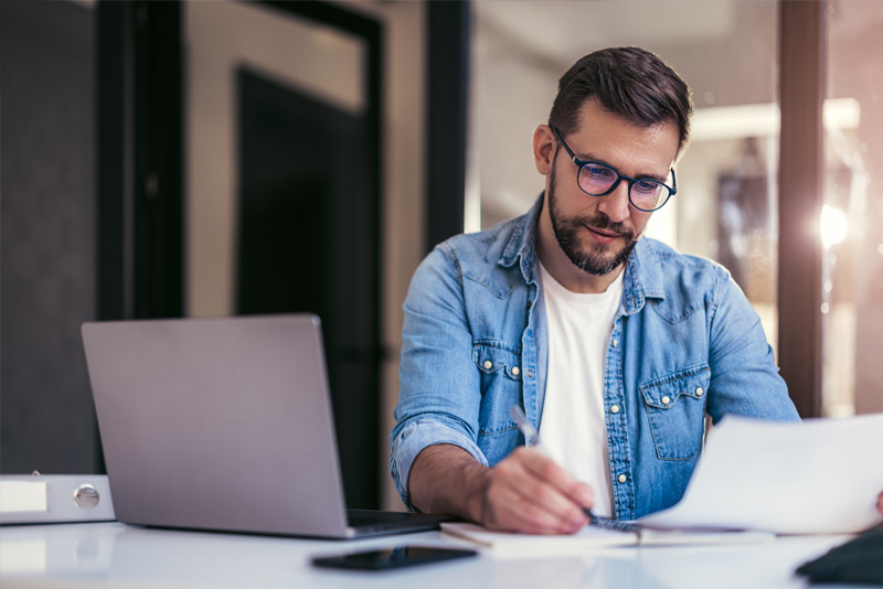 immagine di una persona che sta lavorando con davanti a se aperto un laptop e dei fogli.
