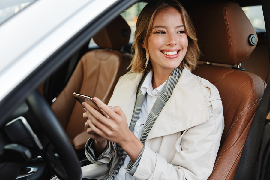 ritratto di una ragazza parcheggiata in macchina che sorride mentre tiene in mano lo smartphone.