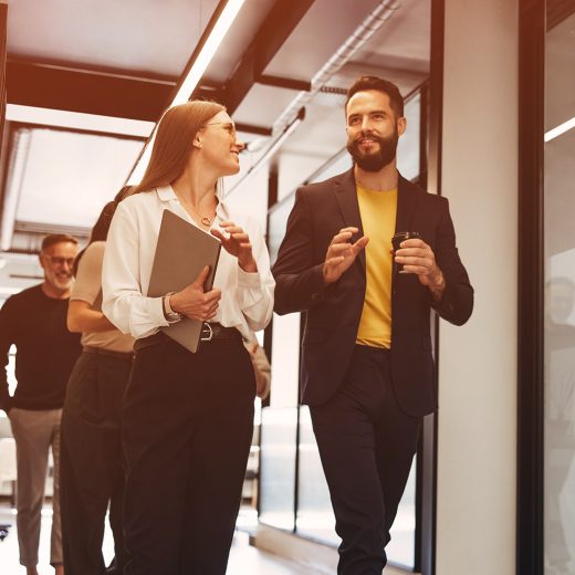 Gruppo di professionisti che cammina e conversa in un ufficio moderno e luminoso, con colleghi in abbigliamento business casual che collaborano e discutono di lavoro nei corridoi di un ambiente aziendale contemporaneo, immagine che rappresenta teamwork, leadership, cultura aziendale, collaborazione professionale e innovazione nel contesto corporate.