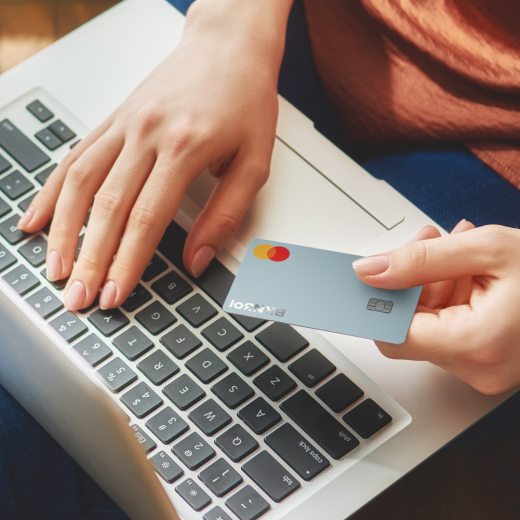 immagine di una persona al computer che tiene in mano una carta 301 credit per effettuare un pagamento online.